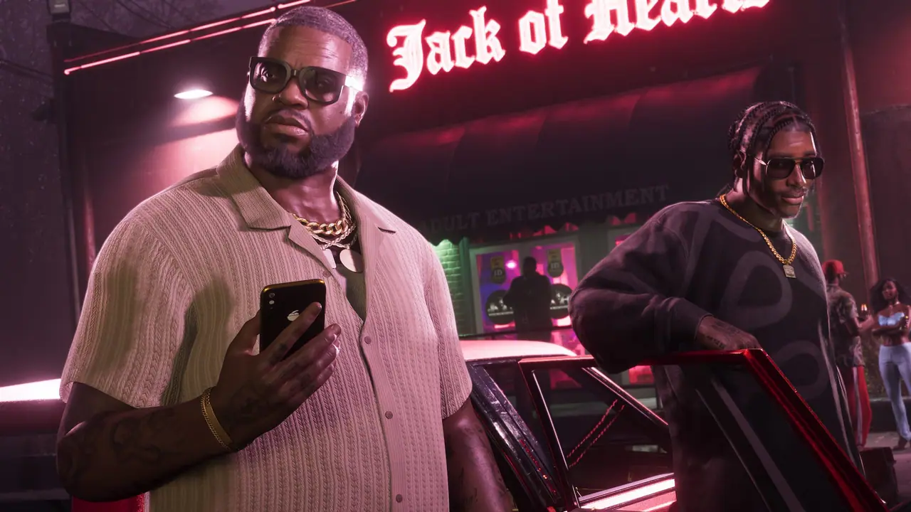 Boobie Ike holding a phone outside the Jack of Hearts club at night, a man in sunglasses leaning on a car behind him
