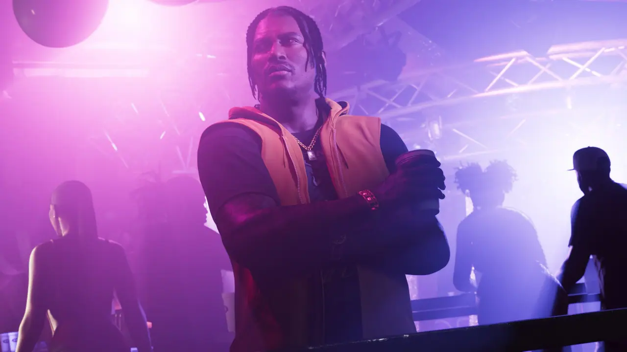 Dre'Quan Priest in an orange vest, arms crossed, in a purple-lit club